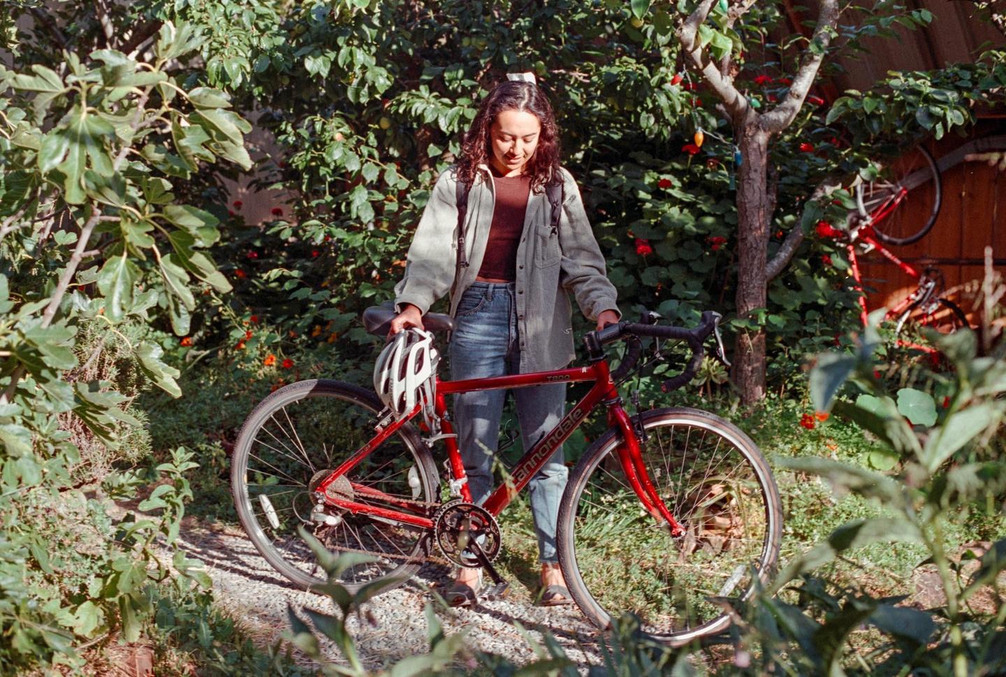 A woman stands with a red bicycle and a white helmet in a lush garden.