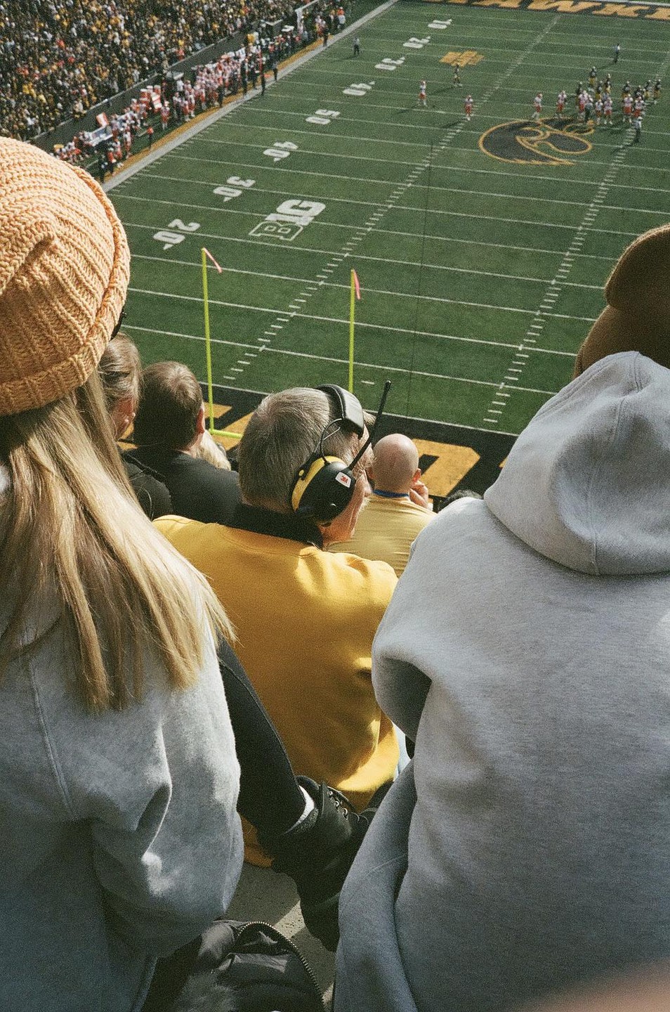 A group of spectators watches a football game from the stands of a stadium.