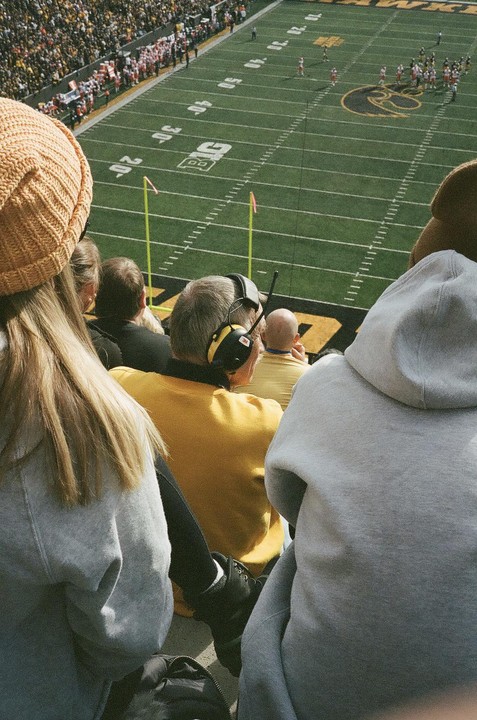 A group of spectators watches a football game from the stands of a stadium.