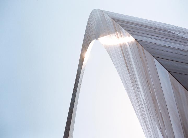The Gateway Arch in Saint Louis is shown from a low angle with the sun flaring through the archway.