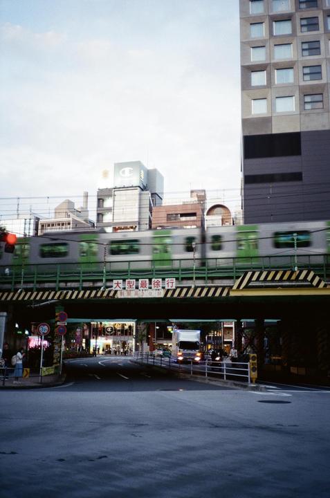 A train passes over a bridge above a street with buildings and vehicles.