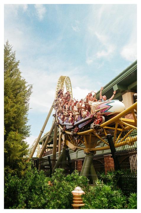 A roller coaster full of people is speeding along a track with a loop against a blue sky.