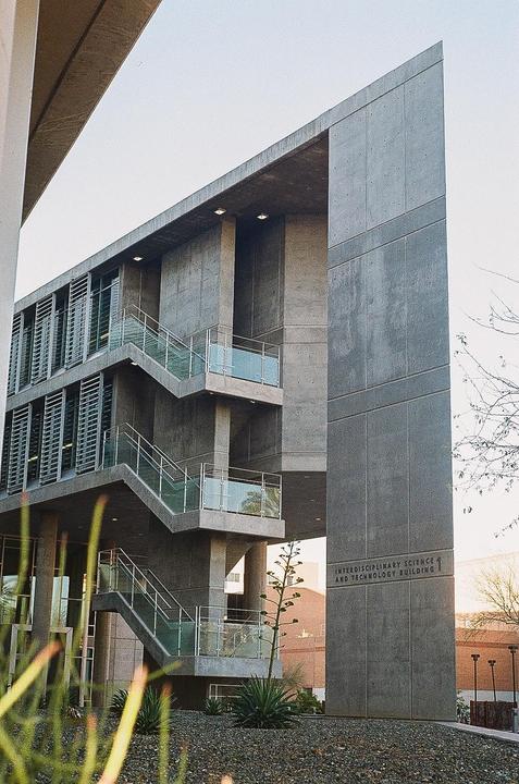 A concrete building with external staircases and glass railings is seen from a low angle.