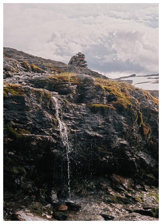 A small waterfall cascades down a mossy, rocky hillside with a stone cairn at the top.