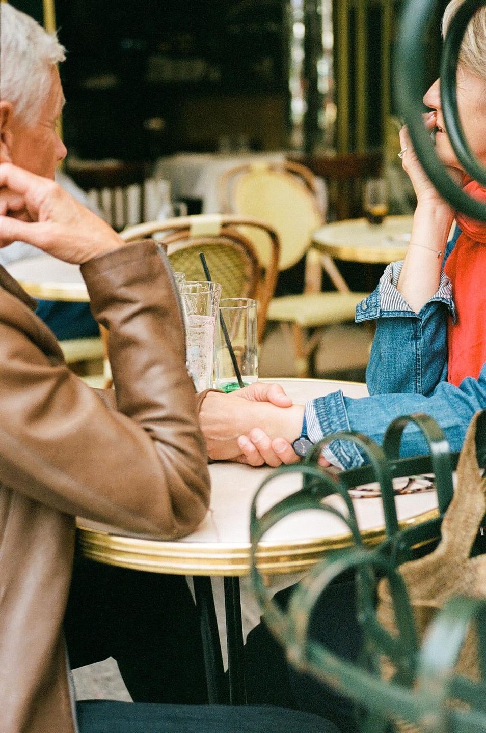 A couple holds hands at a cafe table with drinks.