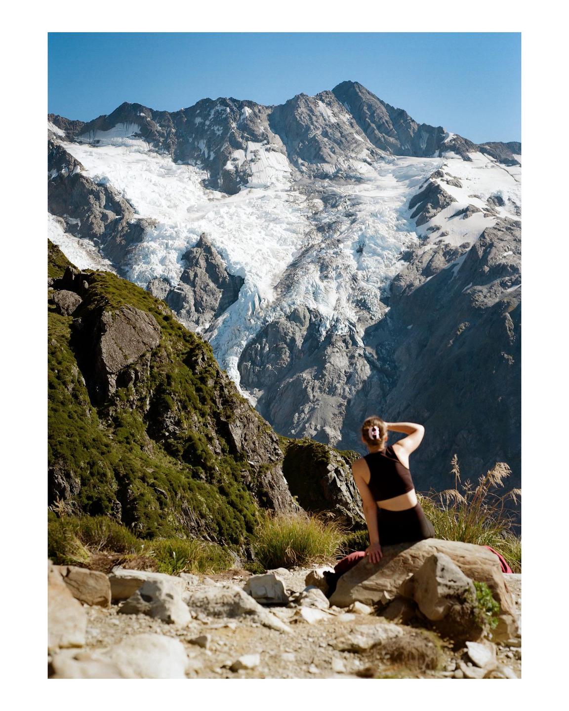 A woman sits on a rock with a large glacier and mountain in the background.