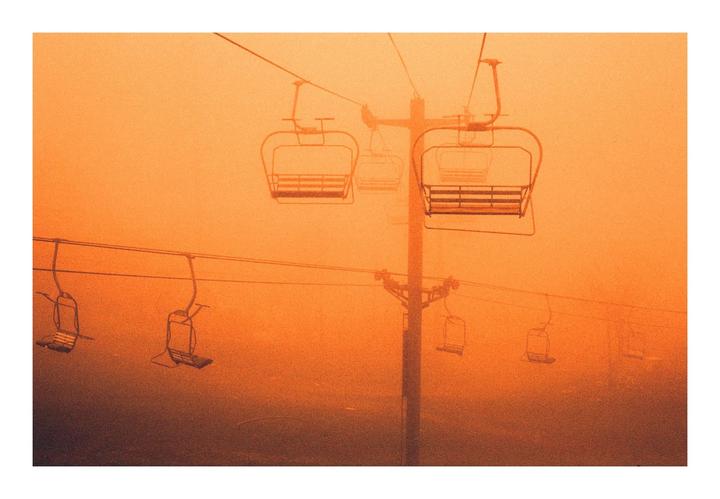 A ski lift with multiple chairs is visible against an orange, hazy sky.
