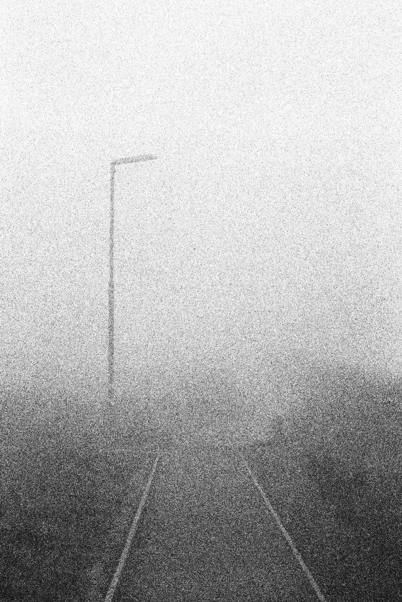 A single street light stands tall above a road disappearing into a thick fog.