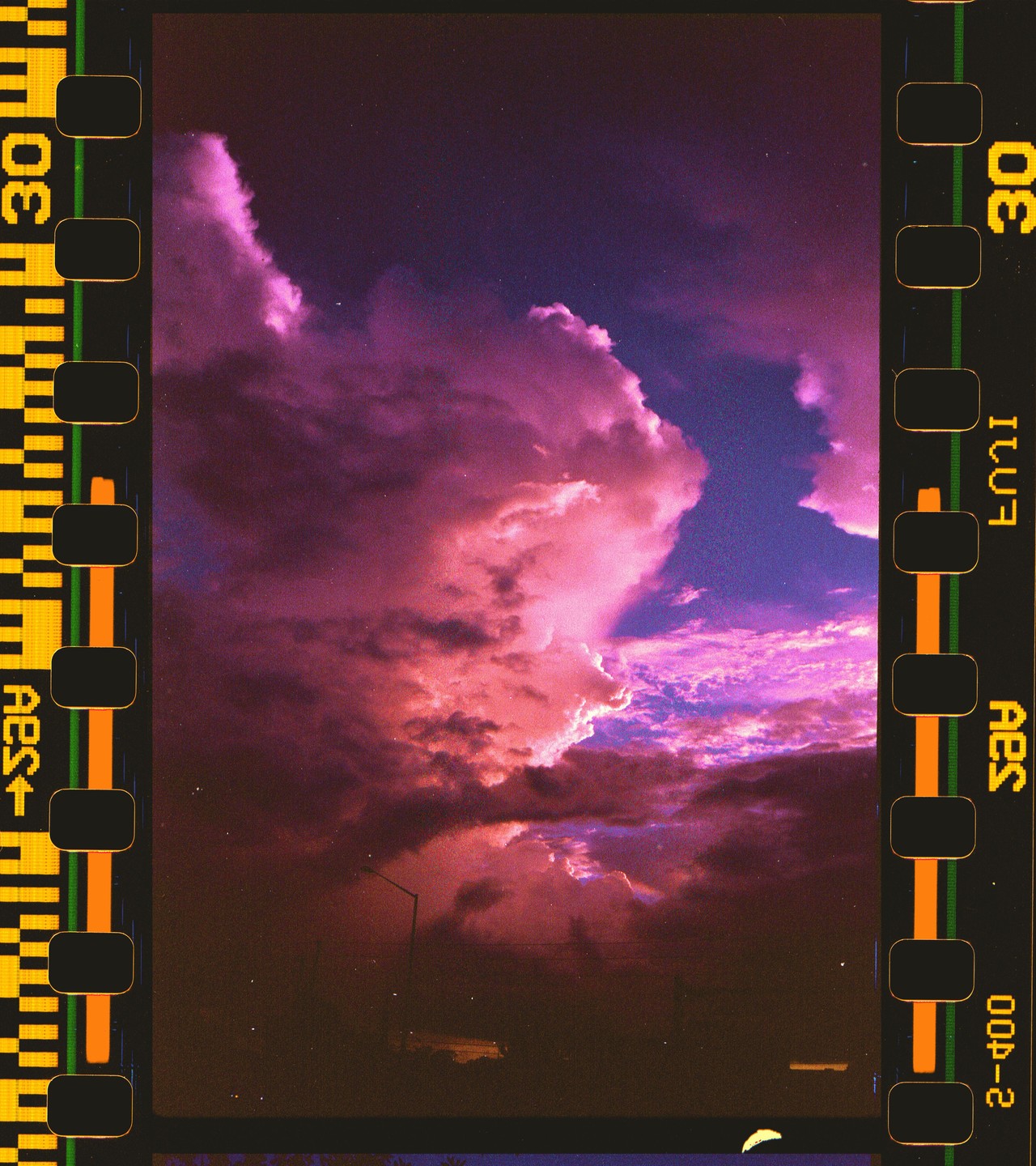 A dramatic sky with vibrant pink and purple clouds is framed by the sprockets of a film strip.