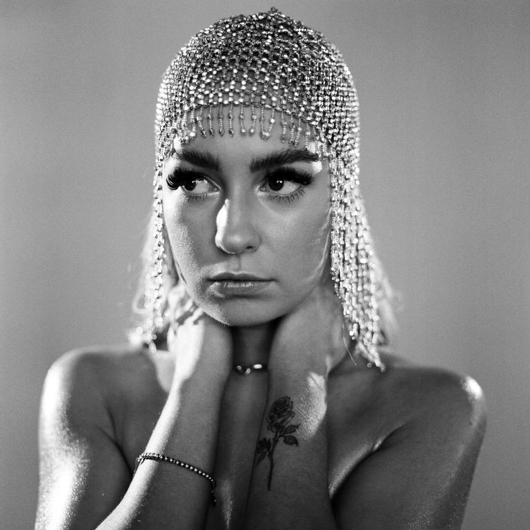 A woman with a beaded headpiece and a rose tattoo on her wrist looks to the side.