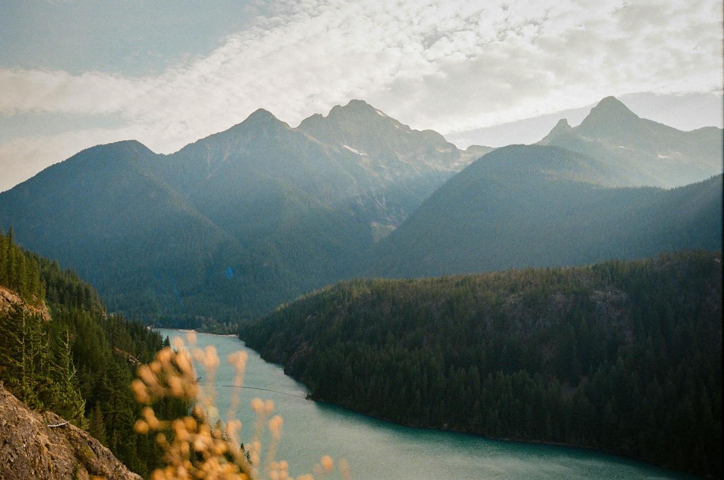 A winding river flows through a valley surrounded by forested mountains under a cloudy sky.