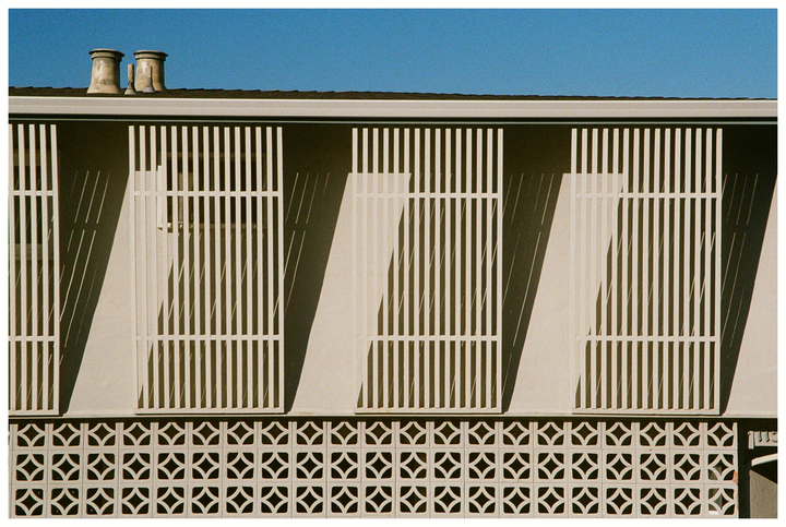A building with vertical white bars and a decorative patterned wall is shown under a clear blue sky.