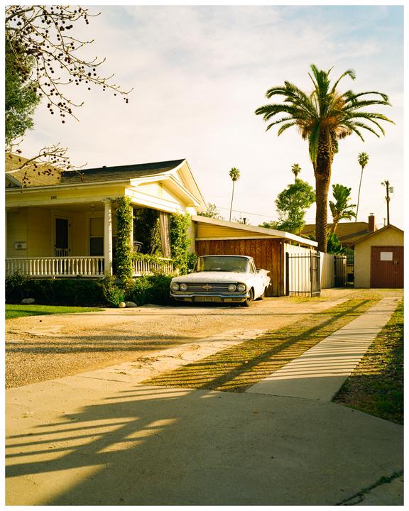 A white car is parked in a driveway next to a house with a palm tree in the background.