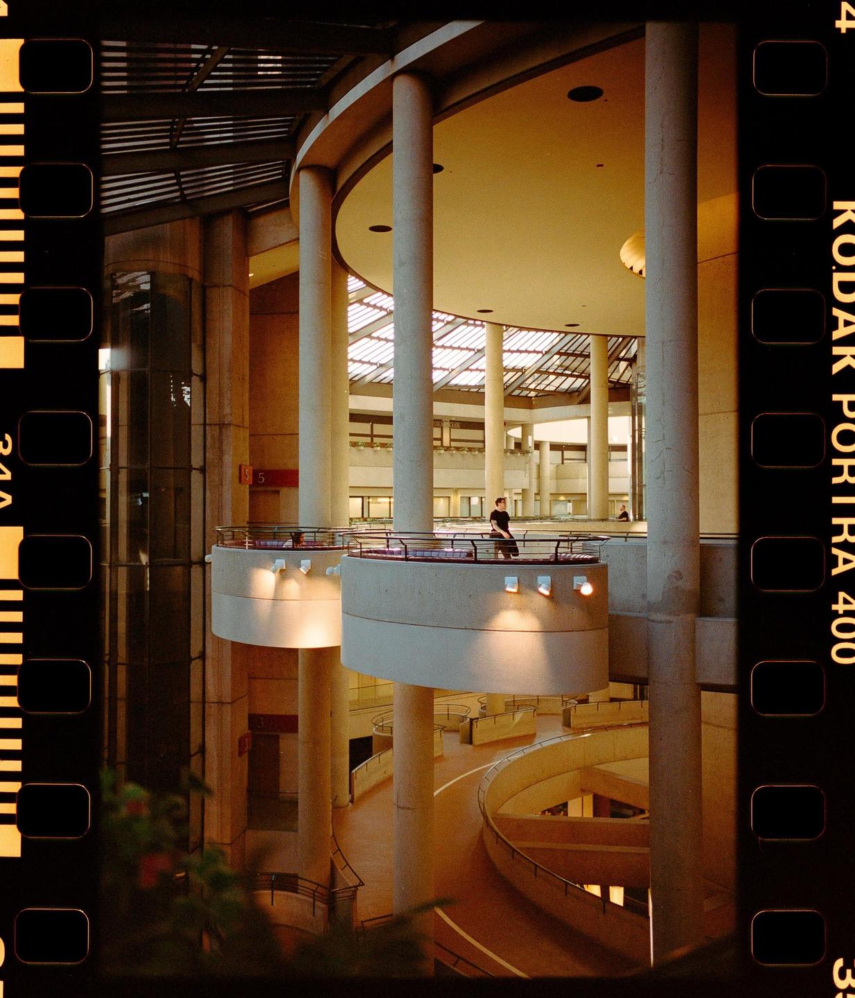 A man stands on a balcony overlooking a multi-story interior space with circular walkways and a skylight.