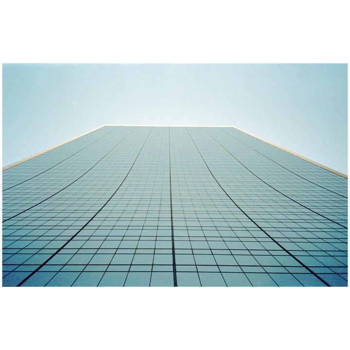 A tall glass building with a grid pattern on its facade rises towards a clear sky.