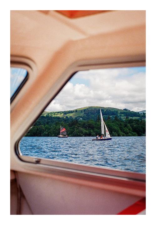 Two sailboats are visible on a lake through a window, with a forested hill in the background.