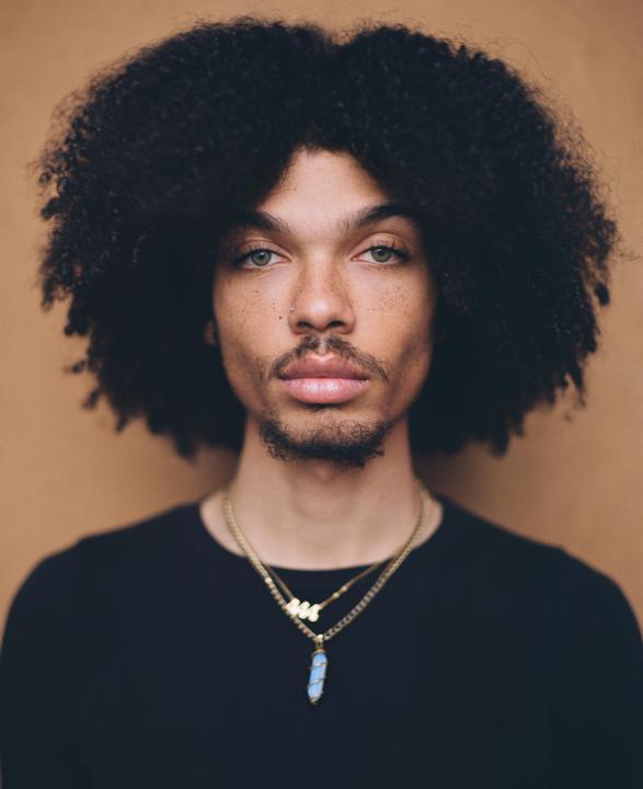 A man with an afro and a beard looks directly at the viewer.