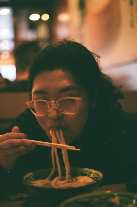 A woman with glasses eats noodles from a bowl with chopsticks.