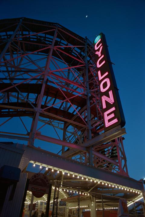 A neon sign for "Cyclone" is visible on a roller coaster structure against a dark blue sky with a crescent moon.