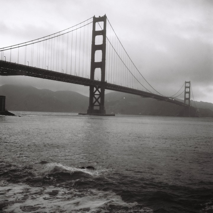 The Golden Gate Bridge spans a body of water with hills in the background under a cloudy sky.