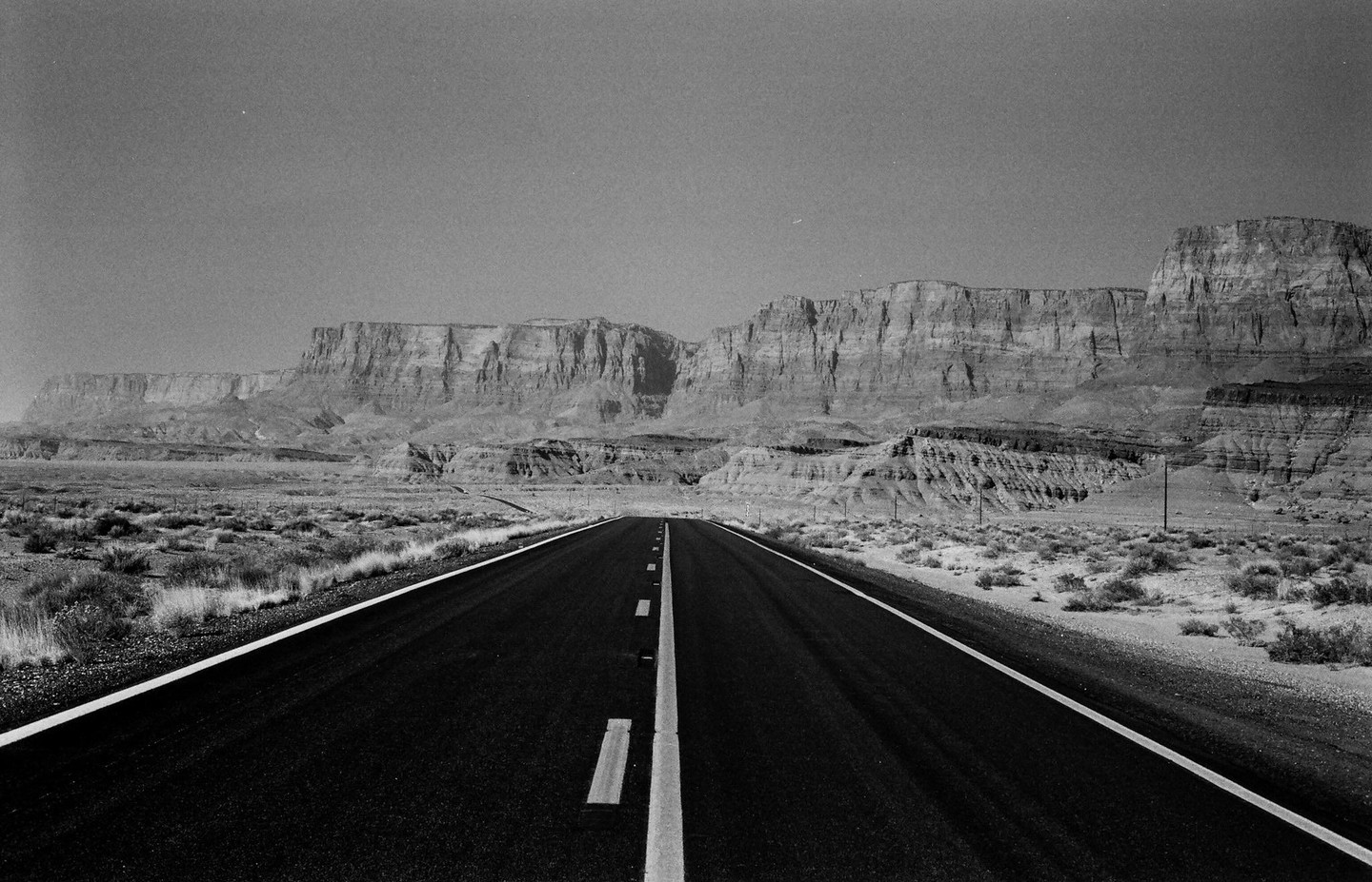 A long desert road stretches towards distant cliffs under a clear sky.