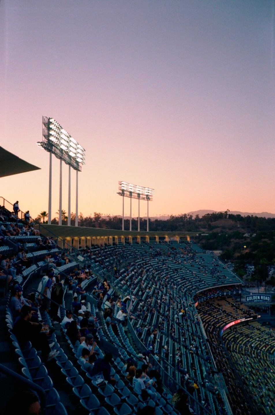 A baseball stadium is filled with spectators under a pink and purple sky at dusk.