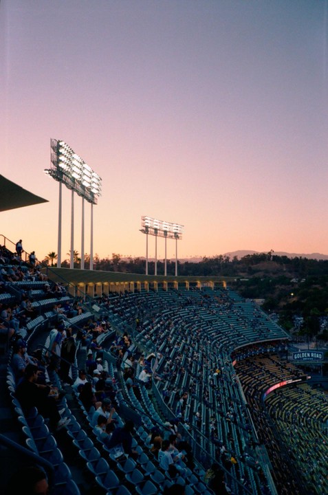 A baseball stadium is filled with spectators under a pink and purple sky at dusk.