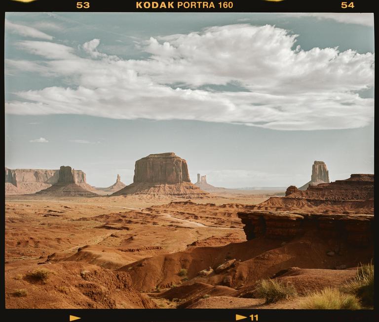 A vast desert landscape features towering rock formations under a cloudy sky.