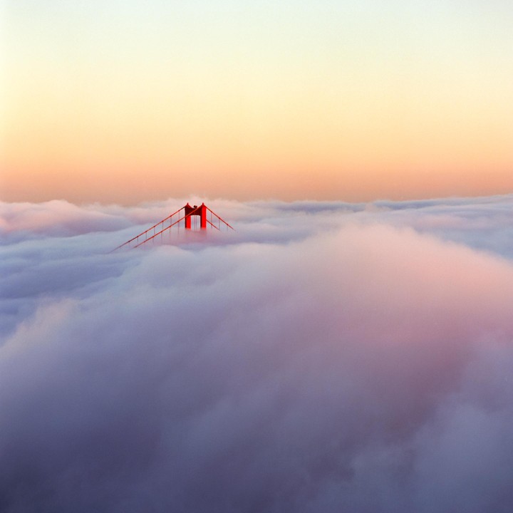 The Golden Gate Bridge is visible above a thick layer of fog at sunset.