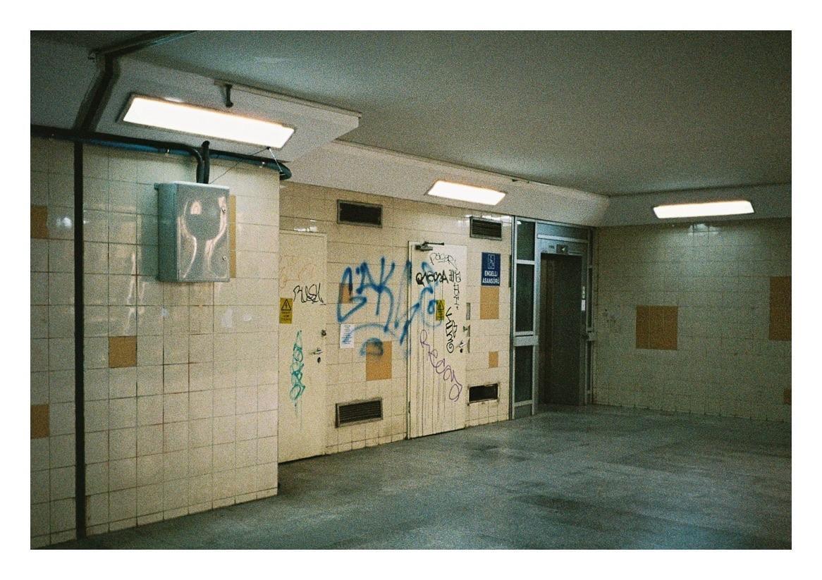 A tiled underground passage with graffiti on the walls and fluorescent lights on the ceiling.