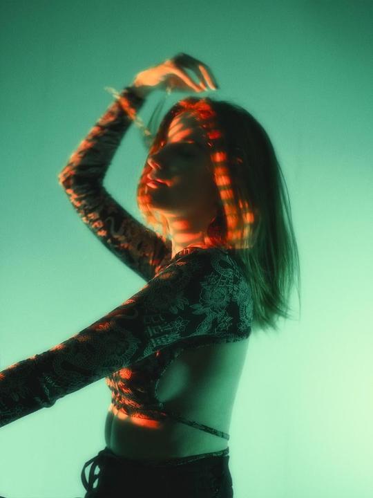 A woman with her arm raised has red light stripes across her face and hair.