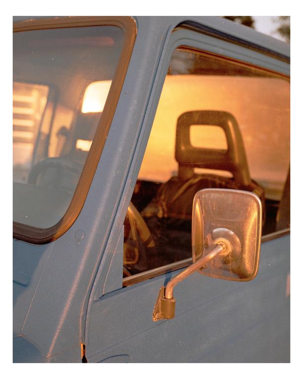 The side of a blue vehicle is visible with a sunset reflected in its windows.