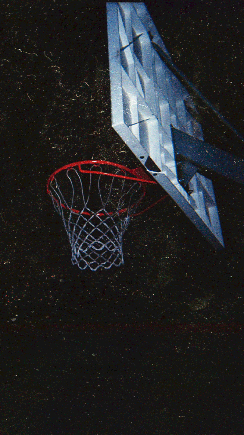 A basketball hoop with a red rim and white net is visible against a dark background.