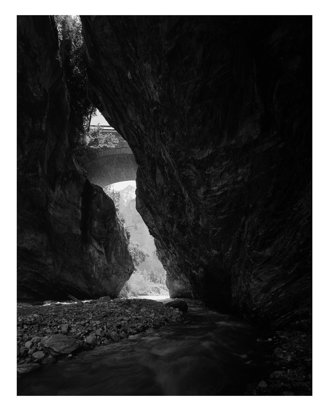A river flows through a dark gorge with a bridge visible above.