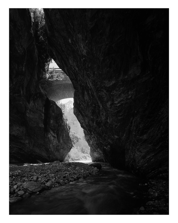 A river flows through a dark gorge with a bridge visible above.