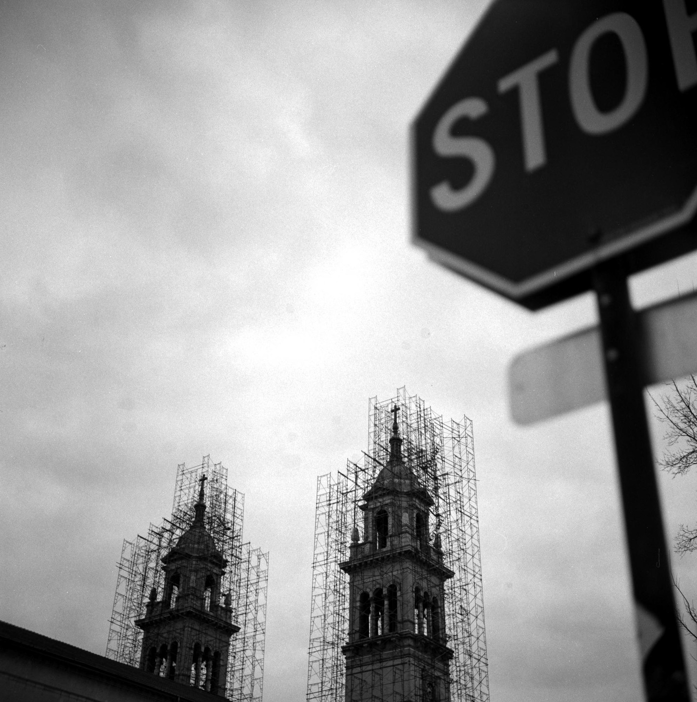 Two church towers covered in scaffolding stand against a cloudy sky, with a blurred stop sign in the foreground.