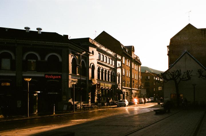 Sunlight reflects off a wet street lined with buildings and cars.