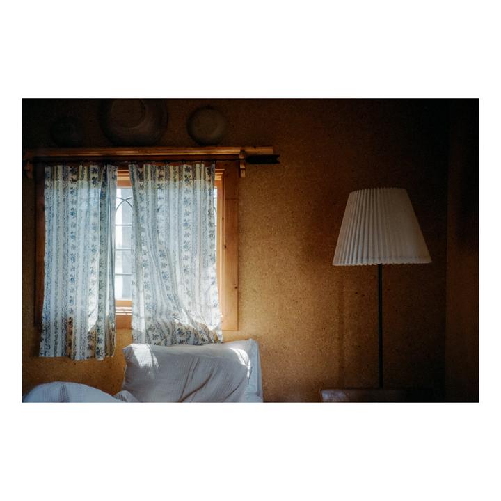 Sunlight streams through a window with floral curtains next to a floor lamp in a room with cork walls.