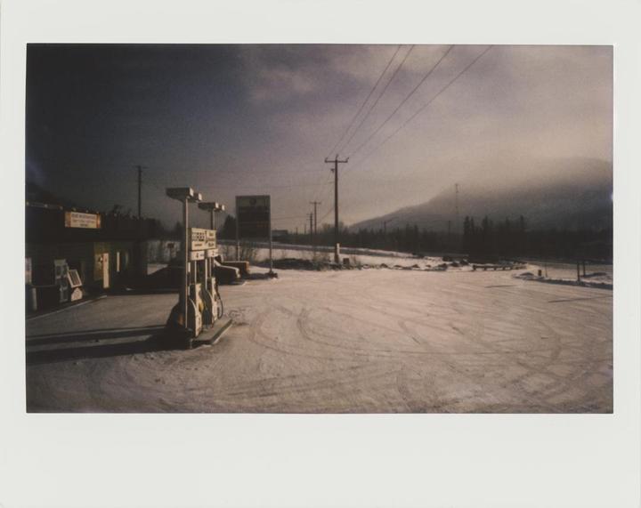 A gas station with snow-covered ground and mountains in the background is visible under a cloudy sky.