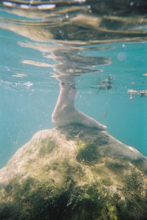 A foot rests on a rock underwater with the surface of the water visible above.