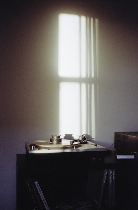 Sunlight streams through a window, casting a shadow of its frame onto a wall above a turntable.