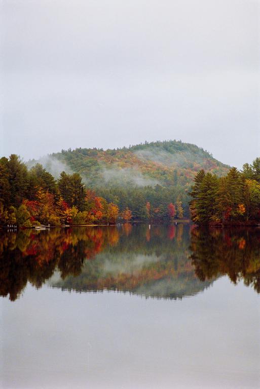 A lake reflects a forest with autumn foliage and a hazy mountain.