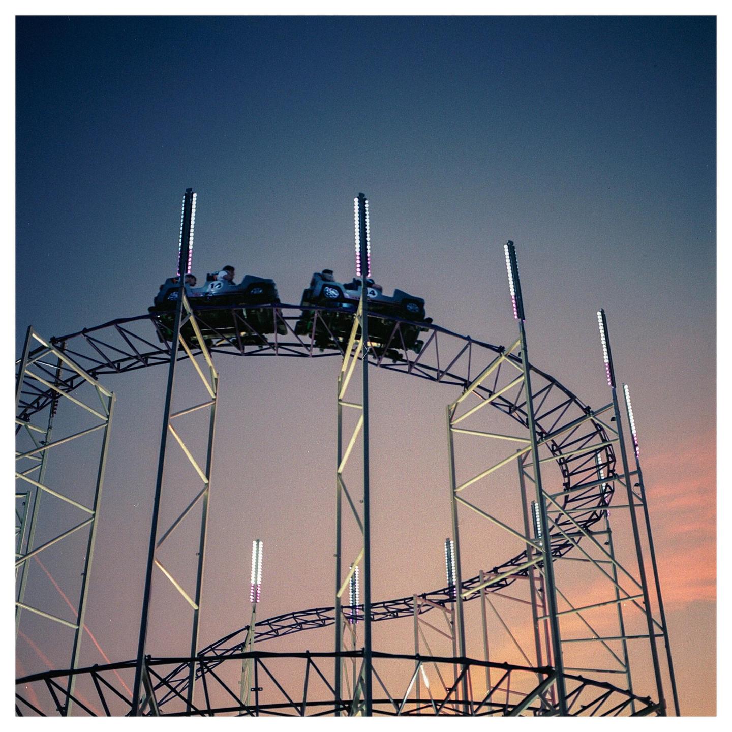 A roller coaster with people in its cars is visible against a twilight sky.