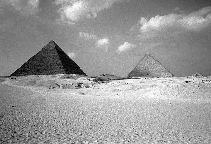 Two pyramids stand in a desert landscape under a cloudy sky.