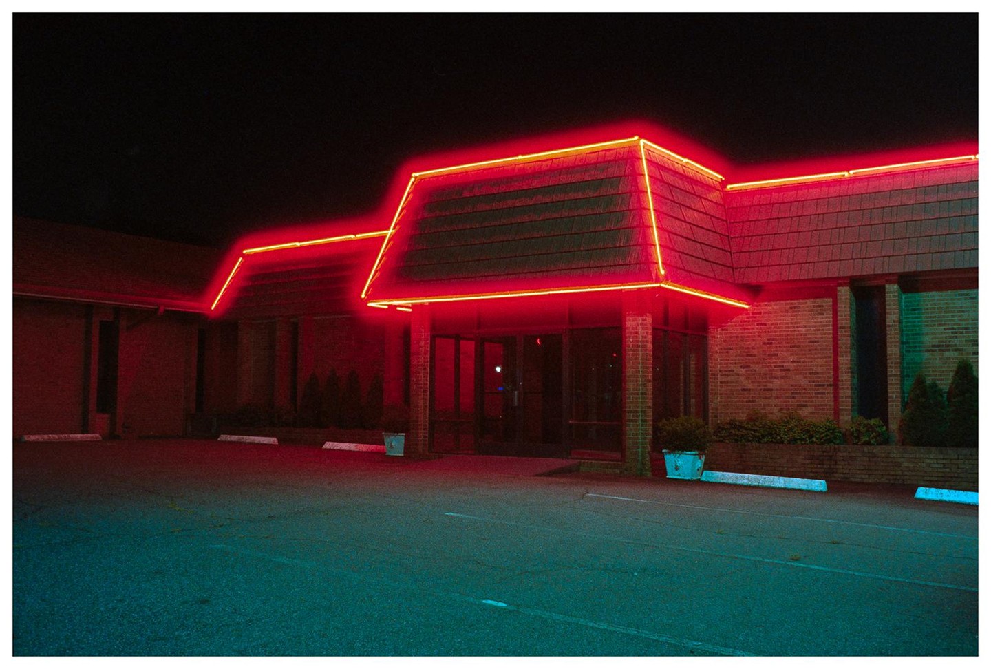 A building with a red neon outline on its roof stands in the dark with a parking lot in the foreground.