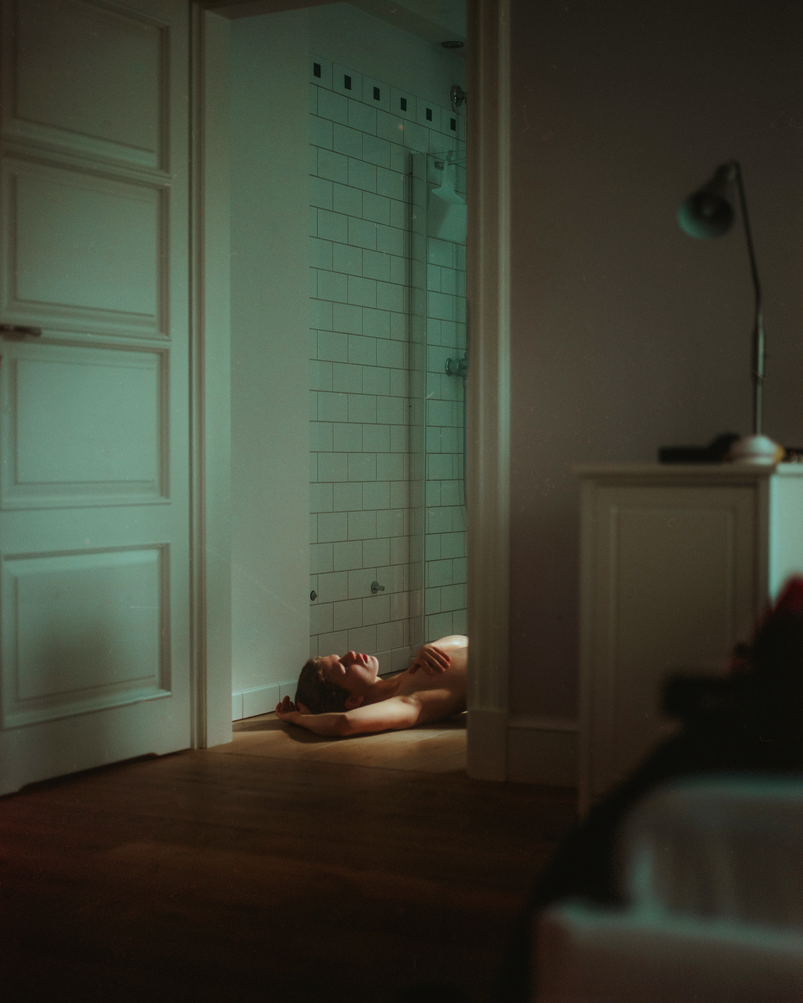 A woman lies on the floor of a bathroom, illuminated by a shaft of light.