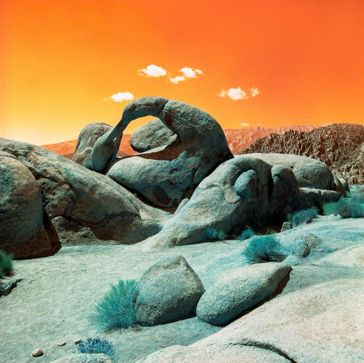 A large rock formation with an arch is visible under an orange sky with two small clouds.