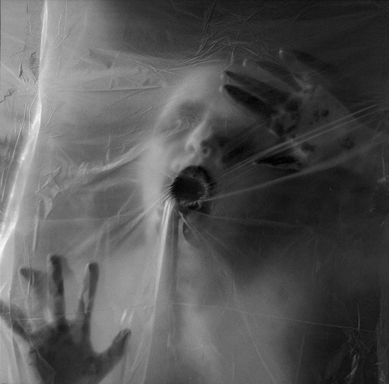A person's face and hands are pressed against a translucent plastic sheet, with their mouth open.