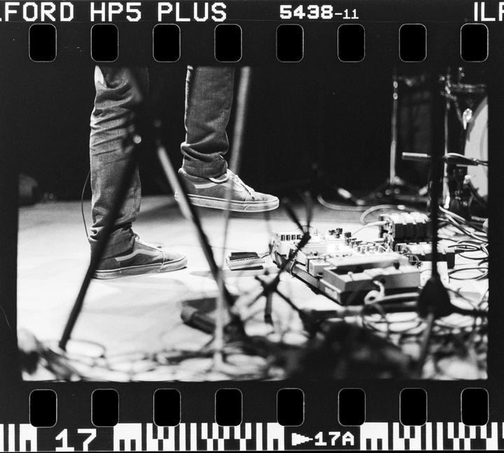 A person's legs and feet are visible on a stage with musical equipment.