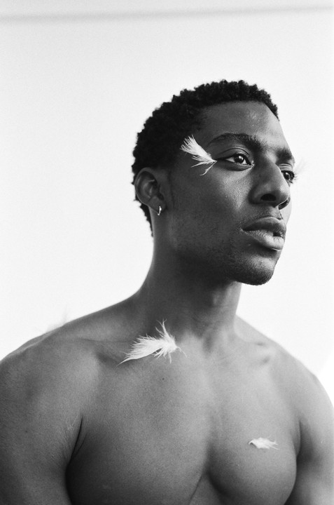 A man with feathers on his face and chest looks to the right.